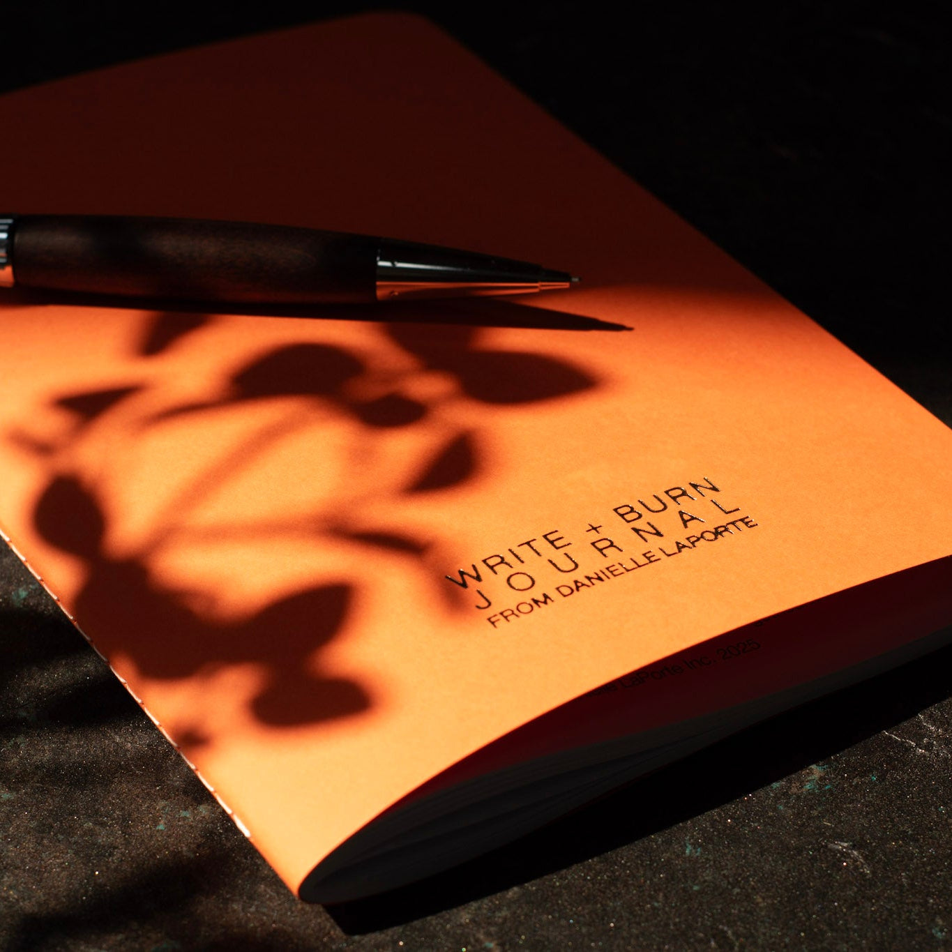 Orange journal with a pen on a dark surface